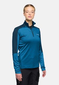 Top atletico turchese con collo a quarto di zip, caratterizzato da accenti a contrasto blu navy sulle spalle e maniche lunghe, realizzato in materiale liscio e leggero.