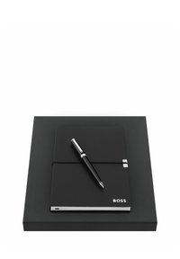 Carnet relié en cuir noir avec bande élastique et stylo argenté sur une boîte noire assortie, marqué "BOSS" dans un coin du carnet.