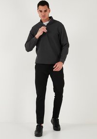 Šedý svetr na zip s žebrovanou strukturou a stojatým límcem, černé slim-fit kalhoty a černé tenisky. Materiál vypadá texturovaně a hladce.