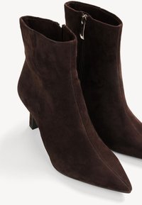 Bottes basses en daim brun foncé avec bouts pointus, talons blocs et fermetures éclair latérales.