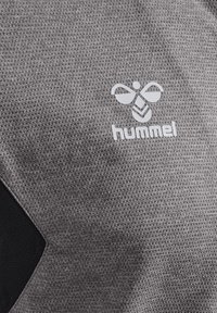 Grå sportsstof med et struktureret mønster; har et hvidt Hummel-logo og en sort accent i et hjørne.