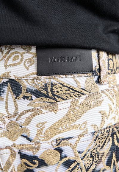 Jeans din denim alb cu modele florale negre și aurii, desfășurate. Prezintă un eticheta de talie din piele neagră, embosată cu "roberto cavalli."
