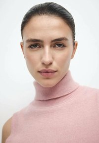 Ružičasti dolčevita džemper od mekog tkanja; krupni plan koji prikazuje glatku teksturu i uzak kroj, naglašavajući izrez i ramena.