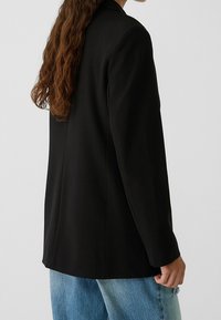 Black blazer with a structured design, featuring a single button closure, notch lapels, and slightly tailored fit. Paired with light blue jeans.