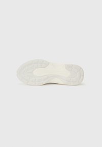 Shoe sole in off-white rubber with textured patterns, featuring indentations and grooves for traction and grip. Smooth upper edge.