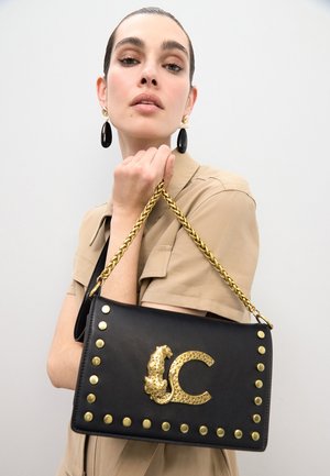 Bolso de mano de cuero negro con detalles de tachuelas doradas y un diseño de leopardo. Cuenta con una correa de cadena y un logo en relieve en forma de "C".