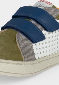 Gros plan sur l'avant d'une basket en daim vert olive, tissu tricot gris, cuir blanc perforé et doubles bandes velcro bleues.