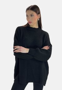 Maglione lavorato a maglia nero con collo alto, vestibilità ampia e polsini a coste. Il tessuto testurizzato e le fessure laterali aggiungono dettagli al design.