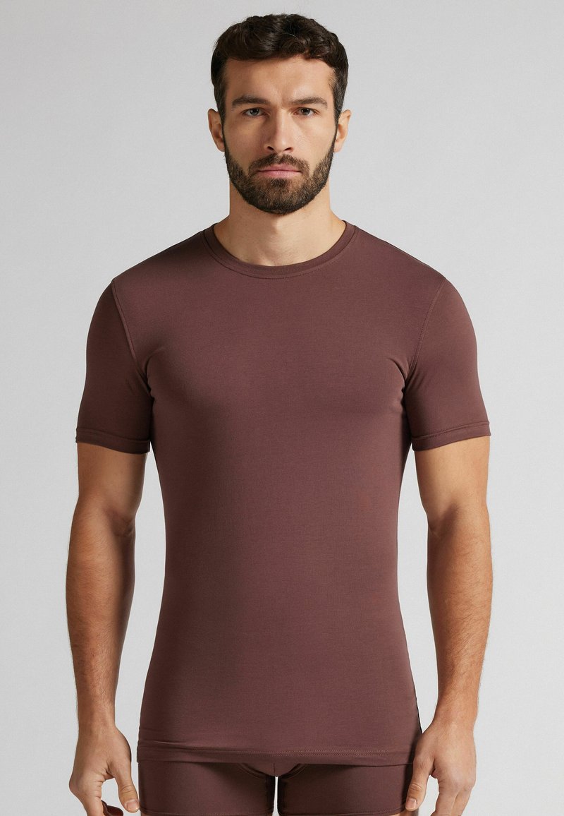 Kawowy, krótki rękaw, dopasowana koszula wykonana z miękkiego, elastycznego materiału. Posiada okrągły dekolt i gładką teksturę.