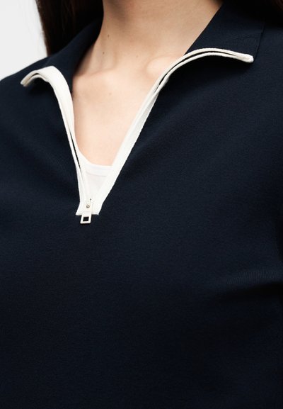 Μπλε ναυτικό πουλόβερ με γιακά μισής ζώνης, λευκό φερμουάρ και άνετη εφαρμογή. Λείο υλικό, μίνιμαλ σχεδιασμός χωρίς εμφανή μοτίβα ή διακοσμητικά στοιχεία.