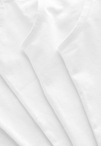 Drie witte katoenen tanktops met een gladde textuur, ronde hals en dunne bandjes, netjes overlappend gerangschikt.