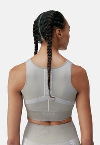 Reggiseno sportivo in morbido tessuto a coste grigio chiaro con dettagli bianchi, caratterizzato da un design senza maniche, una forma aderente e un logo sulla cintura.