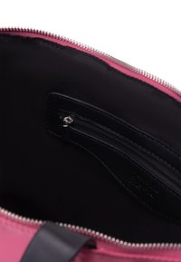 Interno di una borsa rosa, con una fodera in tessuto nero e una tasca con zip dalla consistenza liscia. Accento in argento sulla cerniera superiore.