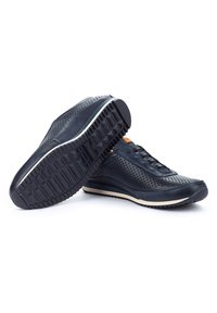 Sneakers perforati blu navy con suola testurizzata e una leggera tonalità chiara per la suola intermedia. Presentano lacci piatti e dettagli sottili.