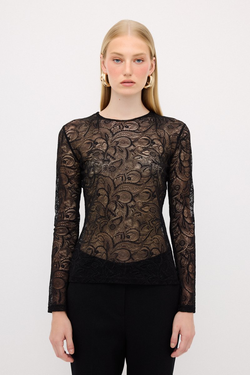 Top in pizzo nero con maniche lunghe, caratterizzato da motivi floreali, scollo rotondo e vestibilità slim. Indossato con pantaloni neri.