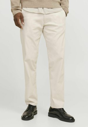 Chinos beige clair en tissu lisse avec une coupe droite. Associés à des chaussures en cuir noires avec des accents détaillés.
