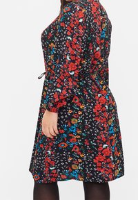 Blumenkleid aus schwarzem Stoff, mit roten, blauen und grünen Blumen, tailliert, langen Ärmeln und einem knielangen Saum.