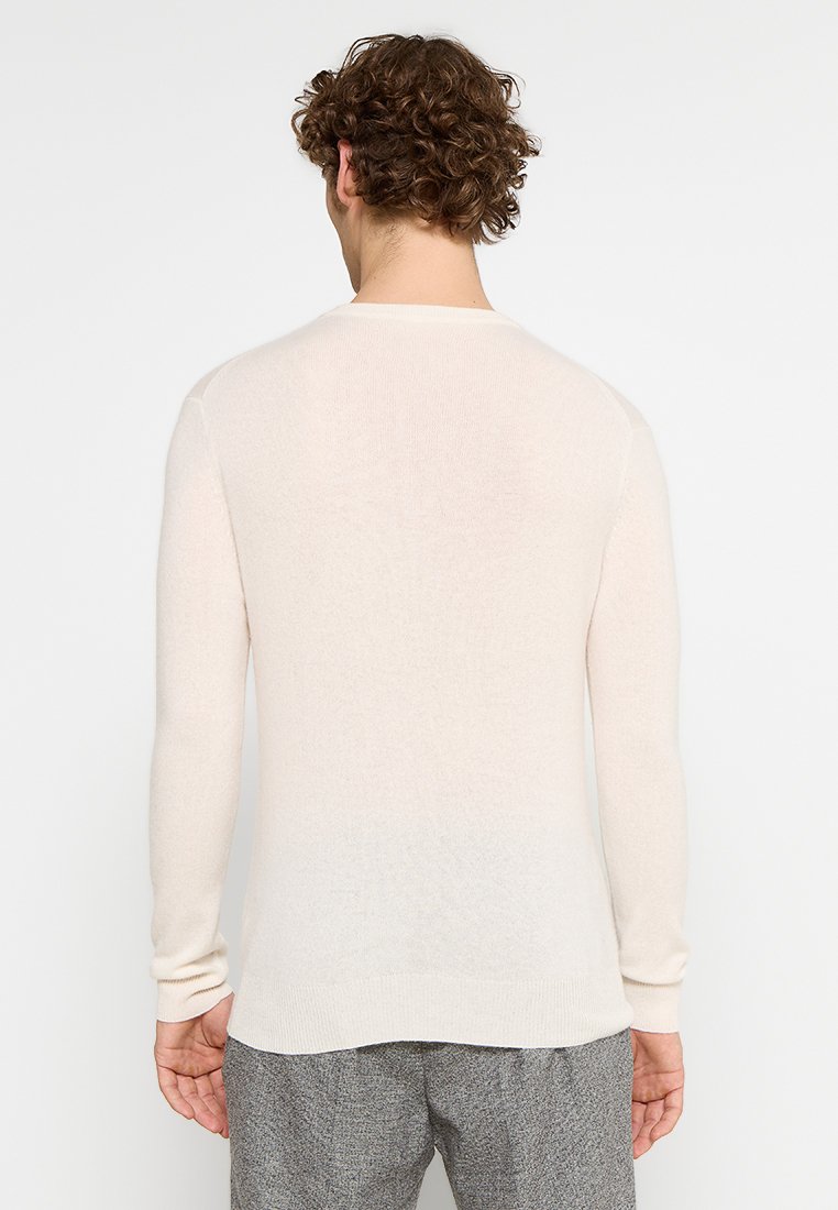 Helles beiges Langarmpullover aus einem weichen, strukturierten Stoff; die Rückansicht zeigt ein nahtloses Design und gerippte Bündchen.