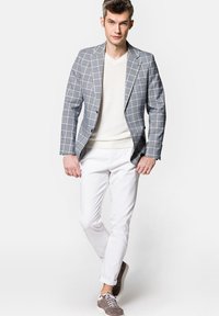 Szary marynarka w kratę noszona na białym swetrze, zestawiona z białymi spodniami i szarymi sneakersami. Cechuje się uporządkowanym designem i kontrastującymi wzorami.