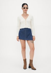 Kremfarget ribbestrikket cardigan med frontknapper, kombinert med en mørkeblå denim miniskjørt med sidelommer, og brune ankelstøvler.