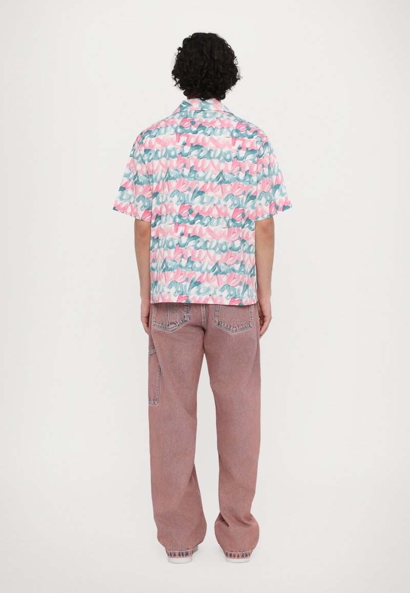 Short-sleeve shirt featuring a multicolored abstract pattern in pink, green, and blue; paired with light red loose-fitting jeans.