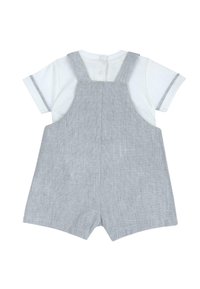 Salopette courte grise avec un t-shirt blanc en dessous. Tissu doux, bretelles réglables et fermeture à boutons au dos pour un habillage facile.