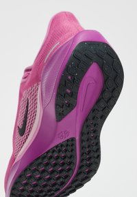 Nike atletska cipela s gornjim dijelom od ružičaste mrežaste tkanine, fleksibilnim ljubičastim srednjim dijelom i teksturiranim crnim gumiranim potplatom s uzorcima za prianjanje.