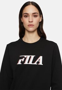 Mustat verkkarit, joissa on pyöreä pääntie, näyttävä valkoinen ja punainen "FILA" -logo rintamuksessa. Pehmeä kangas, jolla on sileä pinta.