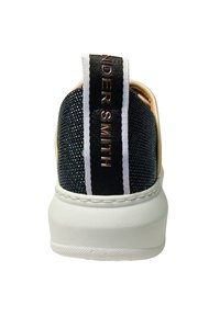 Zwarte en gouden sneaker met een gestructureerde bovenkant, witte accenten, een gevoerde kraag en een opvallende hieltab met branding.