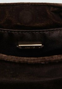 Interno della borsa in camoscio marrone con foderatura liscia, caratterizzato da un'etichetta del marchio metallica cucita e una sottile texture visibile sul tessuto.