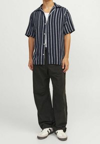 Paski koszula z krótkim rękawem w kolorze granatowym i białym, z kołnierzykiem i zapięciem na guziki, w połączeniu z czarnymi spodniami i białymi trampkami.