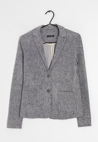 Blazer gris en tissu texturé, avec deux poches avant et deux boutons. Il présente un col cranté et est suspendu à un crochet noir.
