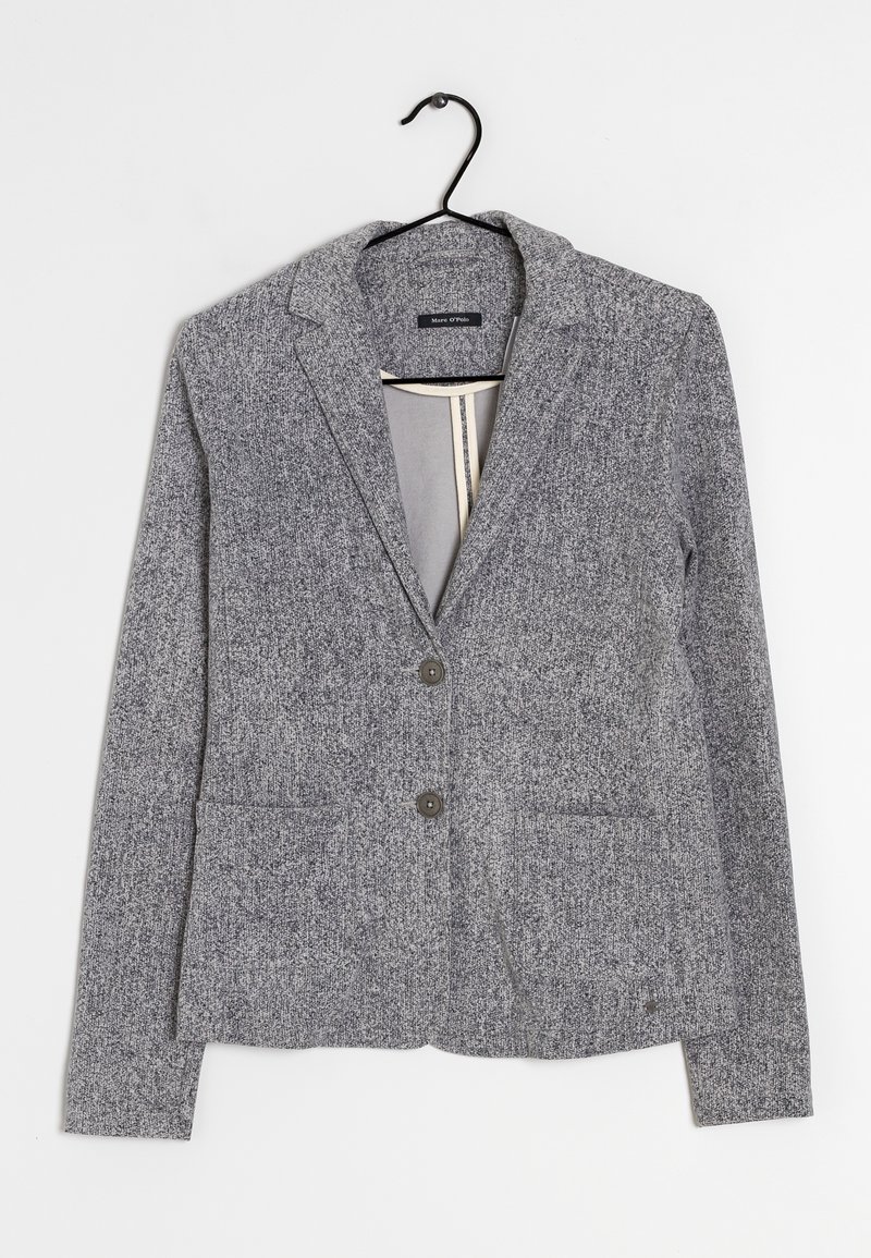 Blazer gris en tissu texturé, avec deux poches avant et deux boutons. Il présente un col cranté et est suspendu à un crochet noir.