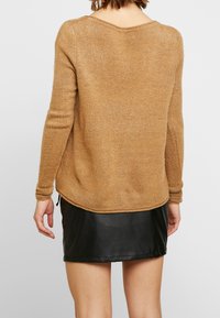 Pull en tricot marron à manches longues et ourlet arrondi, associé à une jupe en cuir noir. Le pull a une texture douce et une coupe décontractée.
