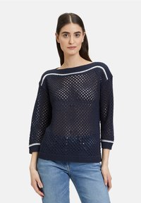 Granatowy sweter dzianinowy z otwartym splotem, szerokim dekoltem, rękawami o długości trzech czwarte oraz białymi akcentami na kołnierzu i mankietach.