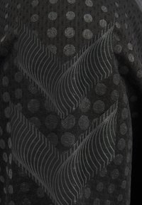 Tissu noir avec des rayures en chevrons texturées et des motifs circulaires de points dans différentes nuances de gris et de noir.