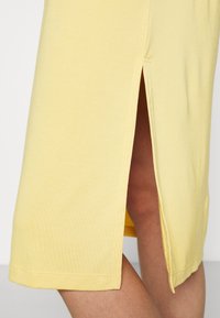 Geel katoenen jurk met een zijsplit, met een gladde textuur en een zoom die net boven de knie valt. Eenvoudig ontwerp en strakke lijnen.