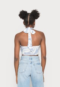 Top cropped com estampa de mármore azul e decote halter, com laço nas costas, feito de um tecido macio, combinado com jeans claros de cintura alta.