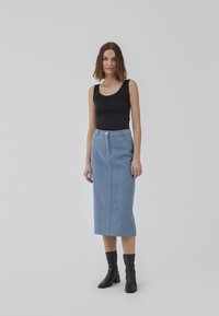 Jupe midi à motif bleu avec fermeture à boutons sur le devant, associée à un débardeur noir ajusté et des bottines noires. Texture de tissu lisse.