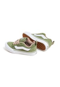 Green suede sneakers with white accents, round toe, and beige laces. Features a textured gum rubber sole and a pull tab at the back.
