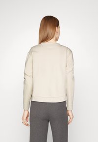 Jasnobeżowa bluza z okrągłym dekoltem i ściągaczami na rękawach, o luźnym kroju i minimalistycznym wzornictwie. Połączona z szarymi spodnie o prążkowanej fakturze.