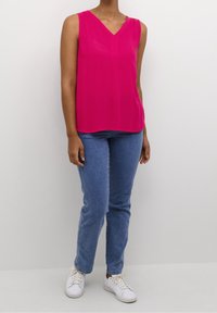 Różowa bezrękawnikowa bluzka z dekoltem w kształcie litery V i gładką teksturą, połączona z jasnoniebieskimi dżinsami o prostych nogawkach i białymi trampkami.