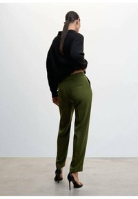 Pull en maille noire, pantalon tailleur vert olive à taille haute et poches arrières, associé à des chaussures à talons noires.