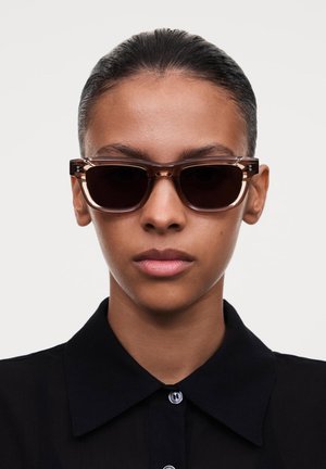 Ochelari de soare tortoise brown cu lentile închise, având o formă rectangulară modernă și accente hardware subtile. Textura pare lucioasă.