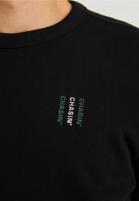 Felpa in cotone nera con scollo rotondo e tre design del testo "CHASIN'" in verde e bianco sul petto.