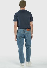Mornarska majica s kratkimi rokavi v kombinaciji z svetlo modrimi denim hlačami, ki imajo rjavo usnjeno oznako na hrbtnem pasu ter bele superge.