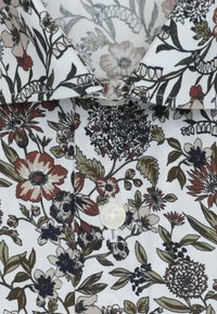 Tissu blanc à imprimé floral multicolore dans des tons de brun, vert et noir, avec un bouton et une partie de col.
