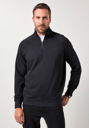 Sudadera negra con cremallera y cuello alto, de textura suave y puños acanalados. Presenta un sutil logotipo en el pecho y un corte relajado.