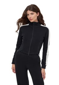 Czarna kurtka zapinana na zamek błyskawiczny z wysokim kołnierzem, białymi paskami po bokach i dwoma przednimi kieszeniami. Miękka tkanina i dopasowany krój, połączona z pasującymi spodniami.