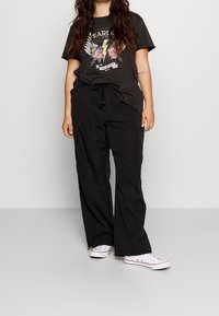 Svarta cargobyxor med elastisk midja och dragsko, tillsammans med en grafisk t-shirt i kolgrått som visar färgglad blixt och rosor.